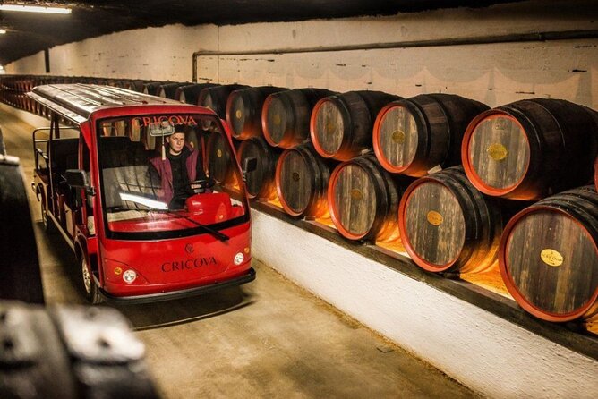 A red tour vehicle drives past massive rows of oak barrels inside the underground Cricova wine cellars.