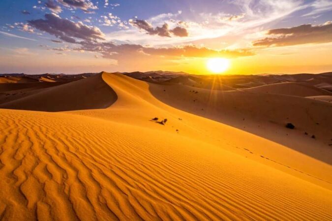 Golden sand dunes under a dramatic sunset sky, inspiring travelers to visit the Sahara.
