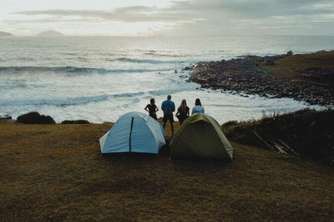 Four campers stand near two tents overlooking the ocean, practicing eco-friendly principles.